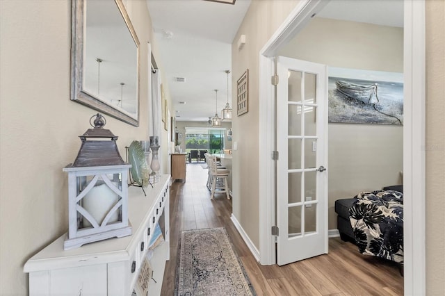 hall featuring visible vents, wood finished floors, baseboards, and french doors