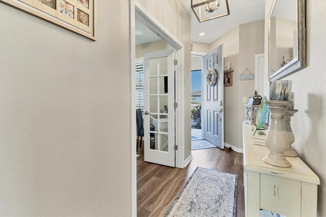 foyer entrance with a chandelier, a textured wall, baseboards, and wood finished floors