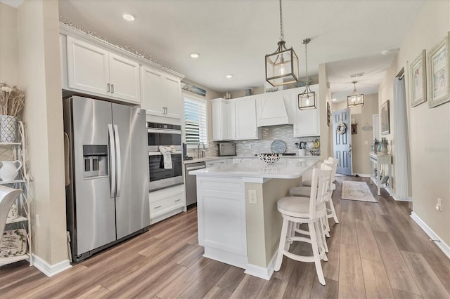 kitchen featuring tasteful backsplash, light countertops, appliances with stainless steel finishes, wood finished floors, and white cabinets