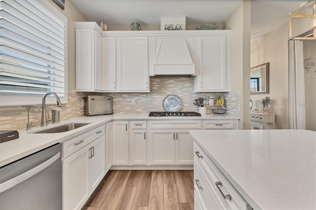 kitchen featuring dishwasher, custom range hood, black cooktop, white cabinets, and a sink