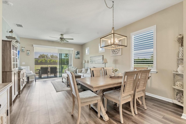 dining room with visible vents, plenty of natural light, wood finished floors, and ceiling fan with notable chandelier