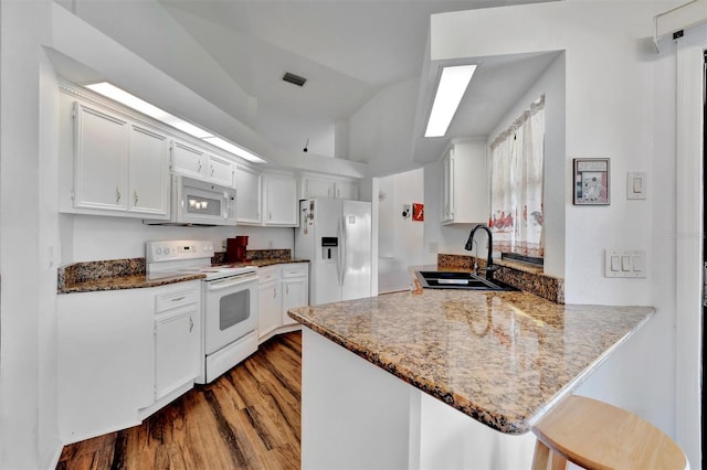 kitchen featuring visible vents, a sink, wood finished floors, white appliances, and a peninsula