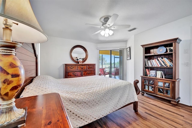 bedroom with a ceiling fan, access to outside, wood finished floors, and visible vents