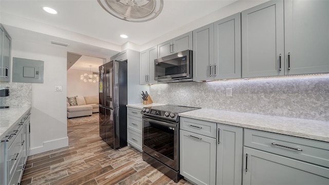 kitchen with wood finish floors, gray cabinetry, backsplash, stainless steel appliances, and a chandelier