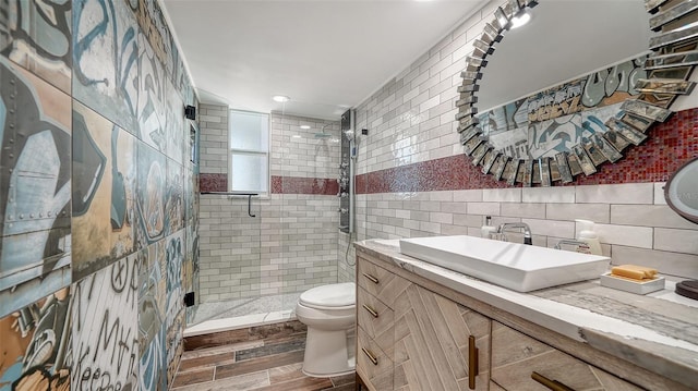 bathroom featuring wood finish floors, toilet, vanity, a stall shower, and tile walls