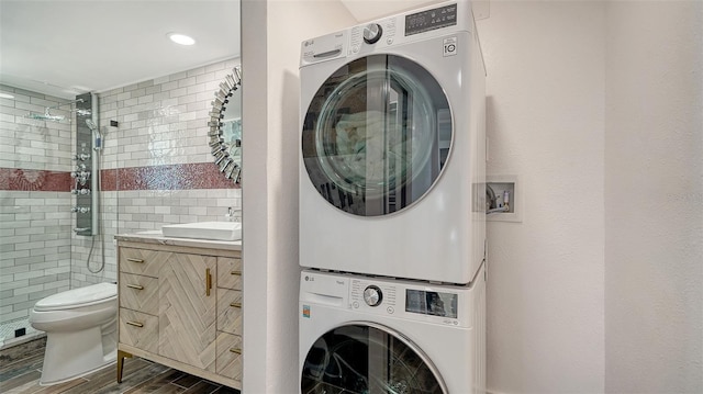 laundry area with a sink, dark wood-style floors, stacked washing maching and dryer, tile walls, and laundry area