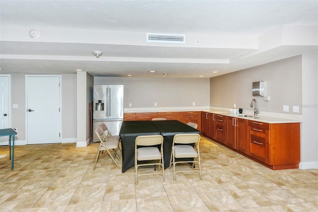 kitchen featuring baseboards, visible vents, stainless steel fridge, and a sink