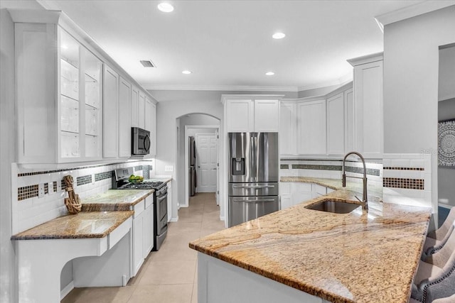 kitchen with light tile patterned floors, a peninsula, arched walkways, a sink, and appliances with stainless steel finishes