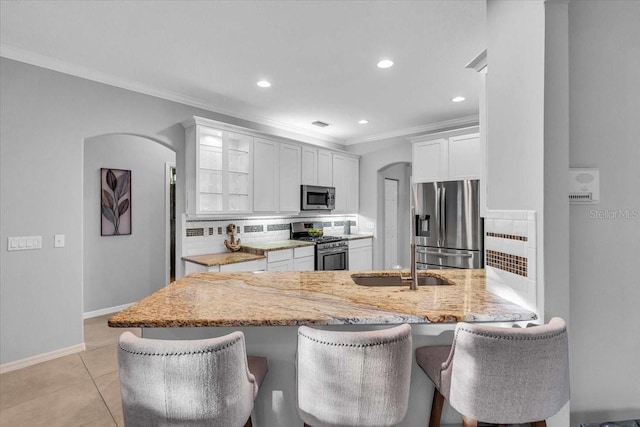 kitchen featuring a breakfast bar, decorative backsplash, a peninsula, arched walkways, and stainless steel appliances