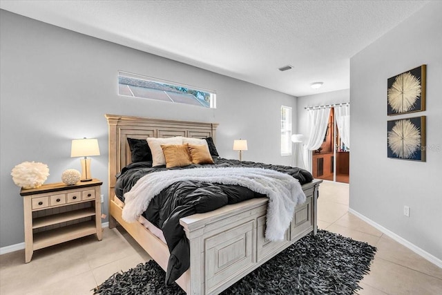 bedroom with light tile patterned flooring, baseboards, visible vents, and a textured ceiling