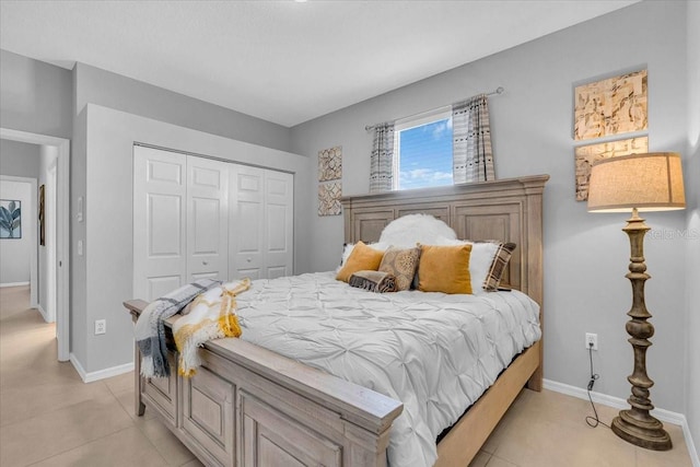 bedroom featuring a closet, light tile patterned floors, and baseboards