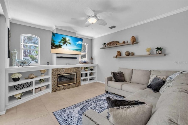 tiled living area featuring a tiled fireplace, a ceiling fan, visible vents, and ornamental molding