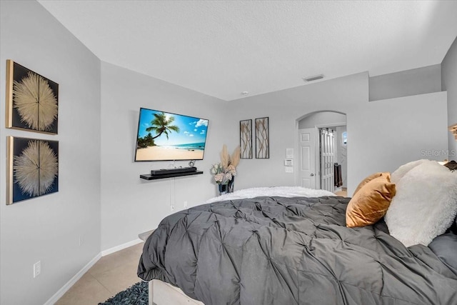 bedroom with a textured ceiling, visible vents, arched walkways, and baseboards