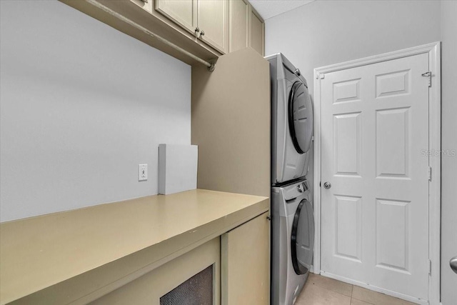 laundry area with light tile patterned floors, cabinet space, and stacked washing maching and dryer