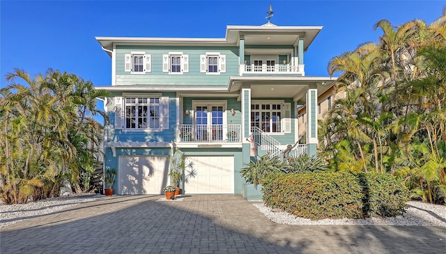 coastal home with a porch, french doors, decorative driveway, a balcony, and an attached garage