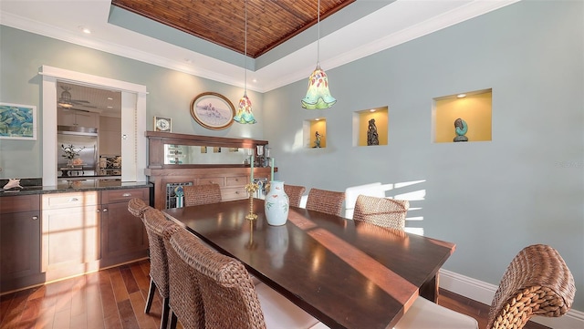 dining area featuring baseboards, dark wood-type flooring, a tray ceiling, and ornamental molding