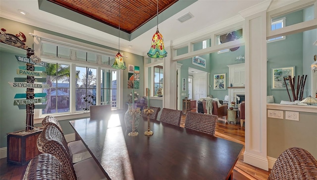 dining room featuring visible vents, ornamental molding, a fireplace, wood finished floors, and a raised ceiling