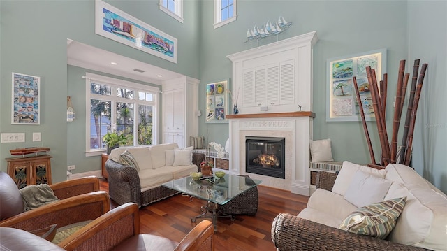 living room featuring a towering ceiling, wood finished floors, baseboards, and a high end fireplace