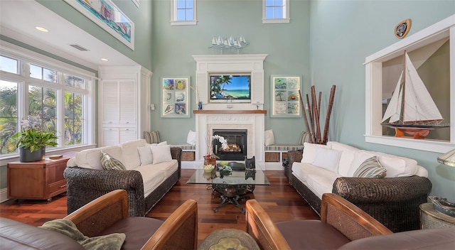 living room with a high ceiling, wood finished floors, visible vents, and a high end fireplace