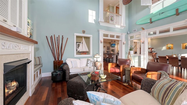 living room featuring visible vents, wood finished floors, a glass covered fireplace, a high ceiling, and baseboards