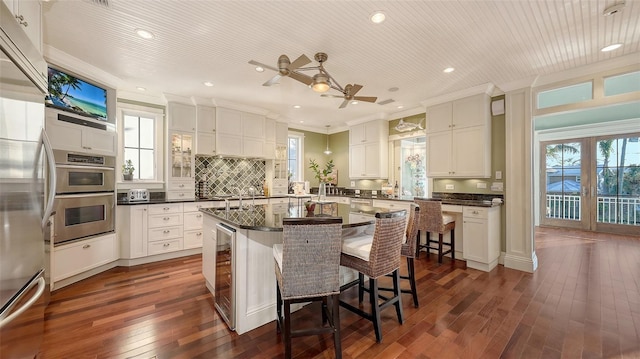 kitchen with dark countertops, tasteful backsplash, a center island with sink, a breakfast bar, and ornamental molding