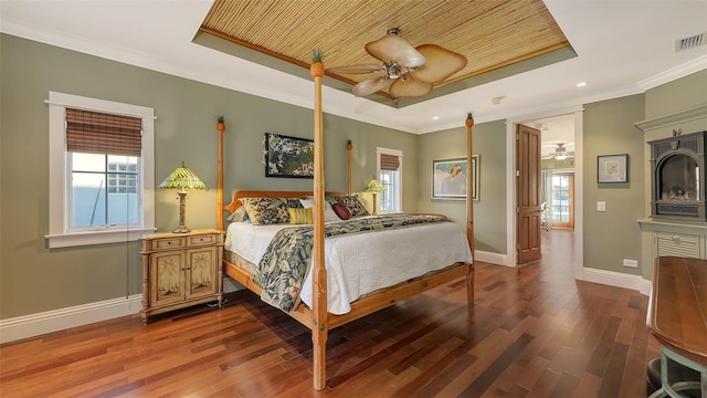 bedroom featuring multiple windows, a raised ceiling, wood finished floors, and ornamental molding