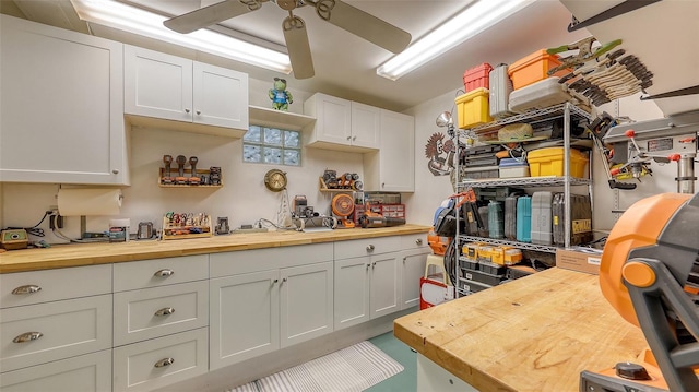 kitchen with butcher block countertops, white cabinetry, and ceiling fan