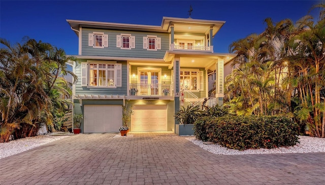 coastal home with a garage, decorative driveway, and a balcony