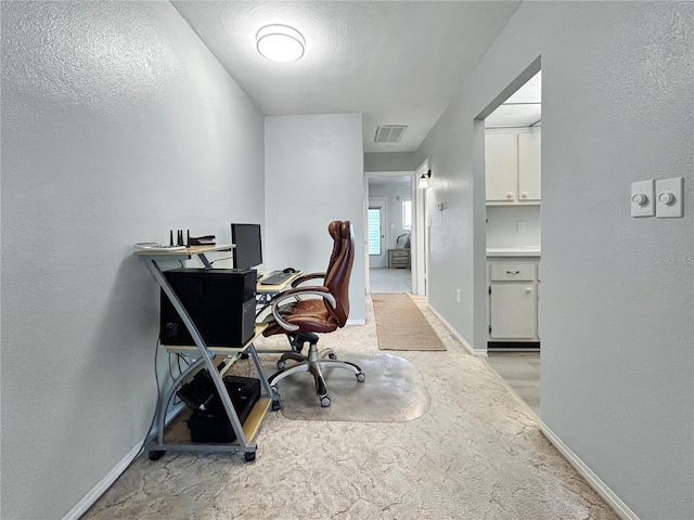 office area with visible vents, a textured ceiling, baseboards, light colored carpet, and a textured wall