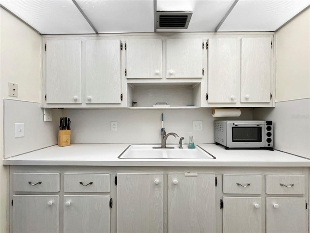 kitchen featuring white microwave, visible vents, a sink, light countertops, and open shelves