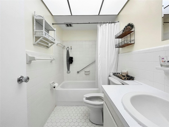 bathroom featuring tile patterned floors, a wainscoted wall, shower / bath combo with shower curtain, toilet, and tile walls