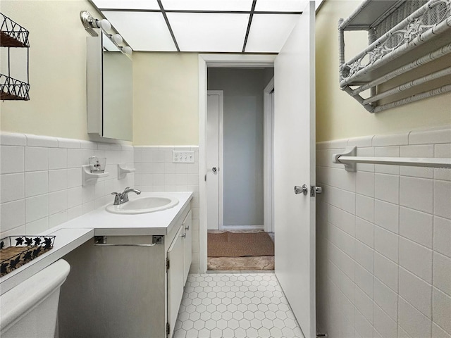 half bathroom featuring tile patterned floors, toilet, tile walls, wainscoting, and vanity