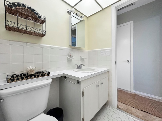 half bath with vanity, visible vents, tile walls, toilet, and tile patterned floors