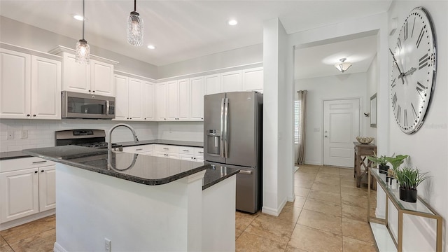 kitchen featuring an island with sink, backsplash, white cabinetry, appliances with stainless steel finishes, and hanging light fixtures