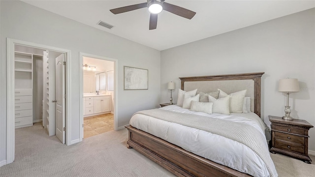 bedroom with visible vents, a walk in closet, baseboards, light colored carpet, and ceiling fan