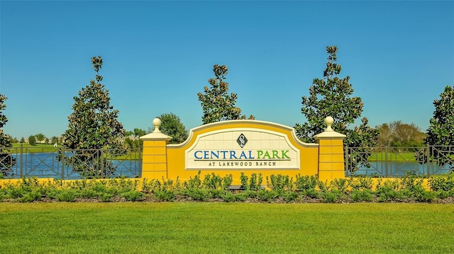 community sign with fence, a lawn, and a water view