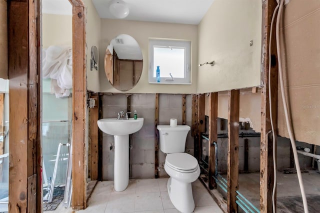 half bathroom with tile patterned flooring, tile walls, toilet, and a sink