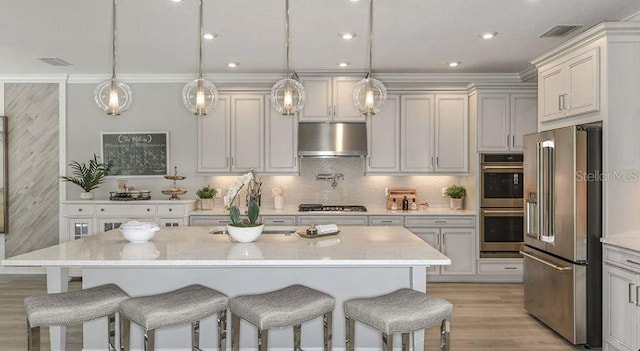 kitchen featuring visible vents, a breakfast bar, under cabinet range hood, appliances with stainless steel finishes, and decorative backsplash