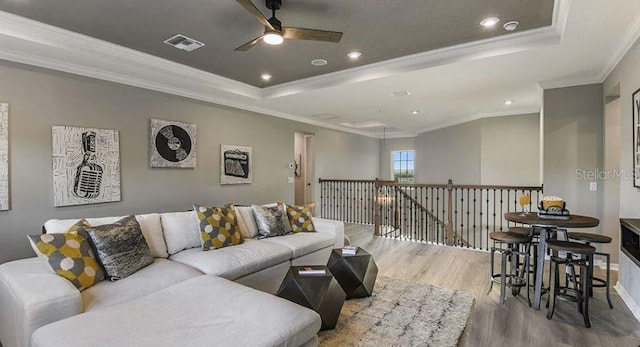 living area featuring a tray ceiling, wood finished floors, visible vents, and ceiling fan