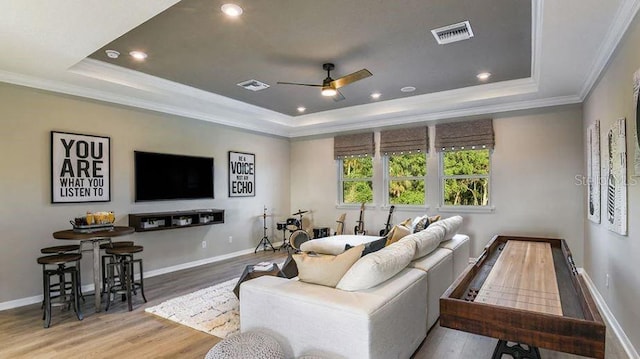 living area with visible vents, ornamental molding, wood finished floors, a raised ceiling, and a ceiling fan