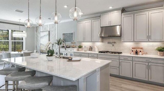 kitchen with under cabinet range hood, stainless steel gas stovetop, gray cabinets, and a sink