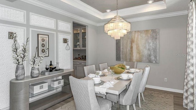 dining area with crown molding, baseboards, wood finished floors, a notable chandelier, and a raised ceiling