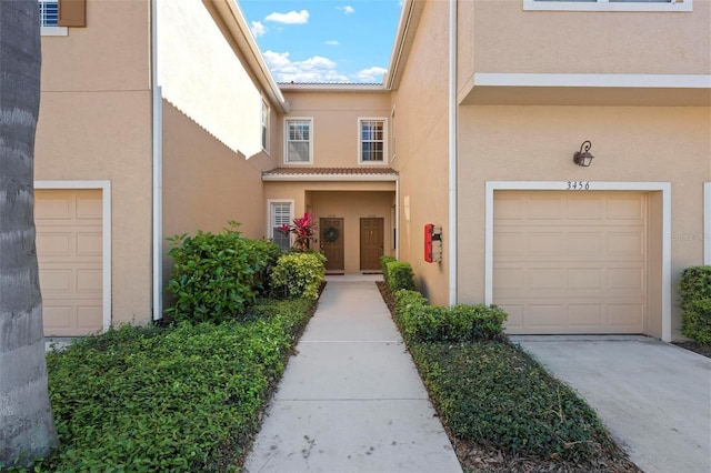 property entrance with concrete driveway, a tiled roof, a garage, and stucco siding