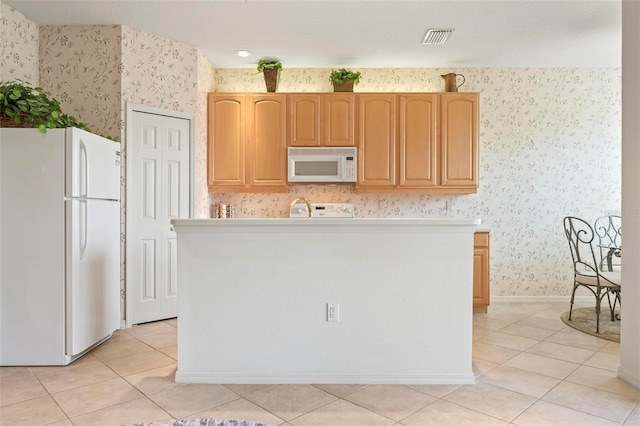 kitchen featuring white appliances, light tile patterned floors, light brown cabinets, a kitchen island, and wallpapered walls