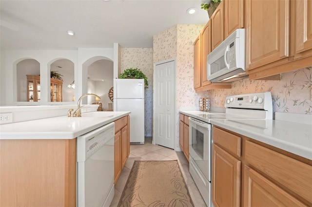 kitchen with wallpapered walls, light countertops, light tile patterned floors, white appliances, and a sink