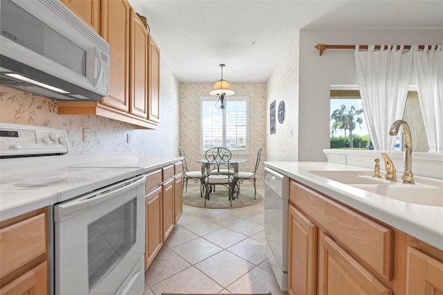 kitchen featuring wallpapered walls, light countertops, light tile patterned floors, white appliances, and a sink