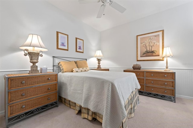 bedroom with ceiling fan, light carpet, and wainscoting