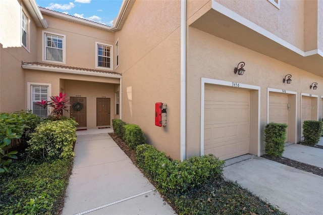 view of exterior entry featuring a tile roof, an attached garage, driveway, and stucco siding