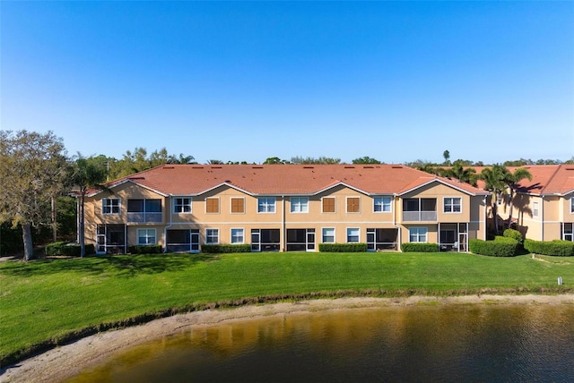 rear view of property with stucco siding, a water view, and a lawn