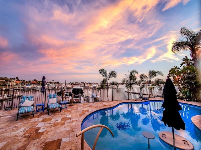 pool at dusk featuring fence, a water view, a fenced in pool, and a patio area